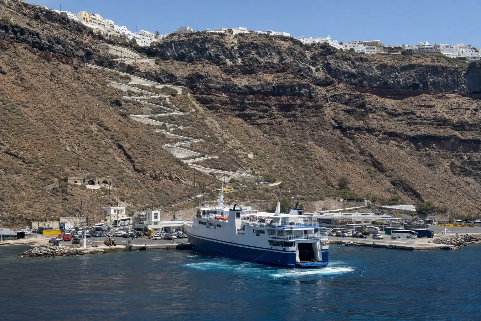 A passenger ferry at Athinios Port beneath Santorini’s steep volcanic caldera cliffs.