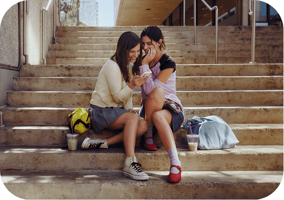 Two students sitting on school steps looking at a phone